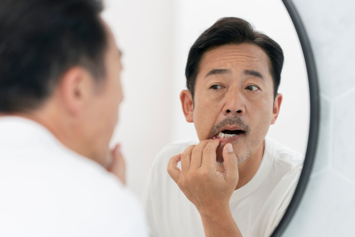 歯周病を気にして鏡で歯茎を確認しているミドル男性